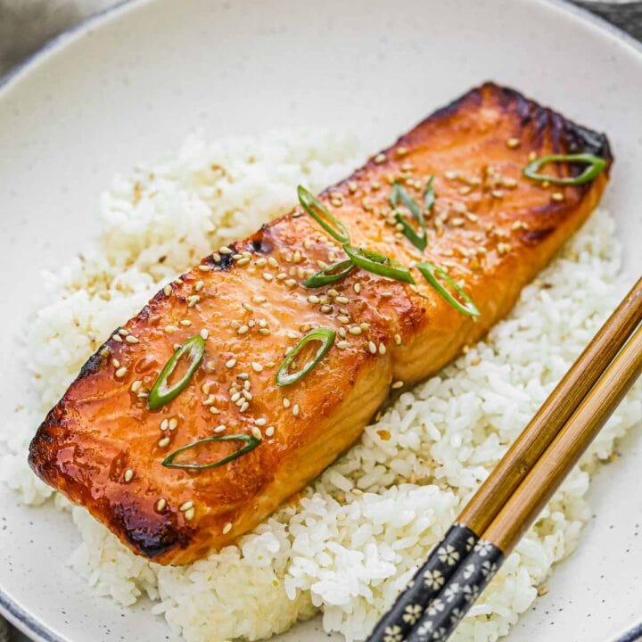 Broiled miso-glazed salmon on a bed of Japanese rice topped with toasted sesame seeds and scallions and served with chopsticks.