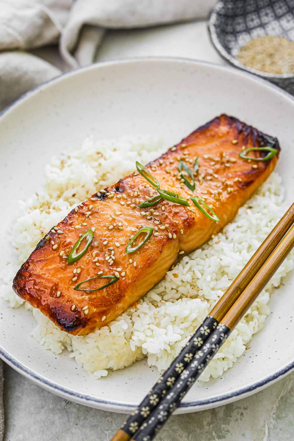 Broiled miso-glazed salmon on a bed of Japanese rice topped with toasted sesame seeds and scallions and served with chopsticks.