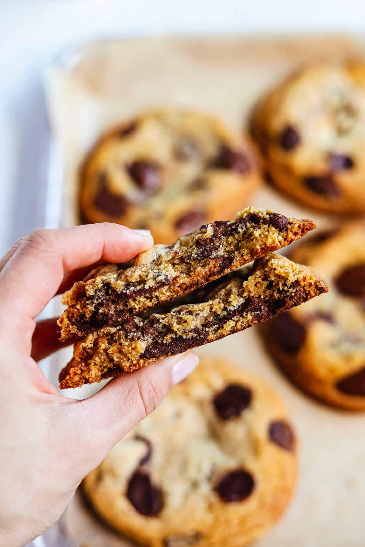 Hand holding a stack of giant bakery-style chocolate chip cookies cut in half to show the melted chocolate inside.