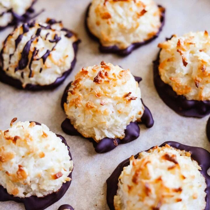 Gluten-free coconut macaroons drizzled and dipped in chocolate on a sheet pan.