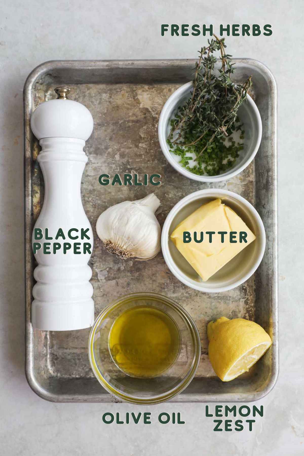 Ingredients to make roasted herb garlic butter, like high-quality butter, fresh herbs, garlic, olive oil, lemon zest, and black pepper.