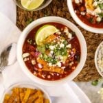 Healthy hearty turkey chili with crispy corn tortillas, cotija cheese, lime, and cilantro in white bowls.