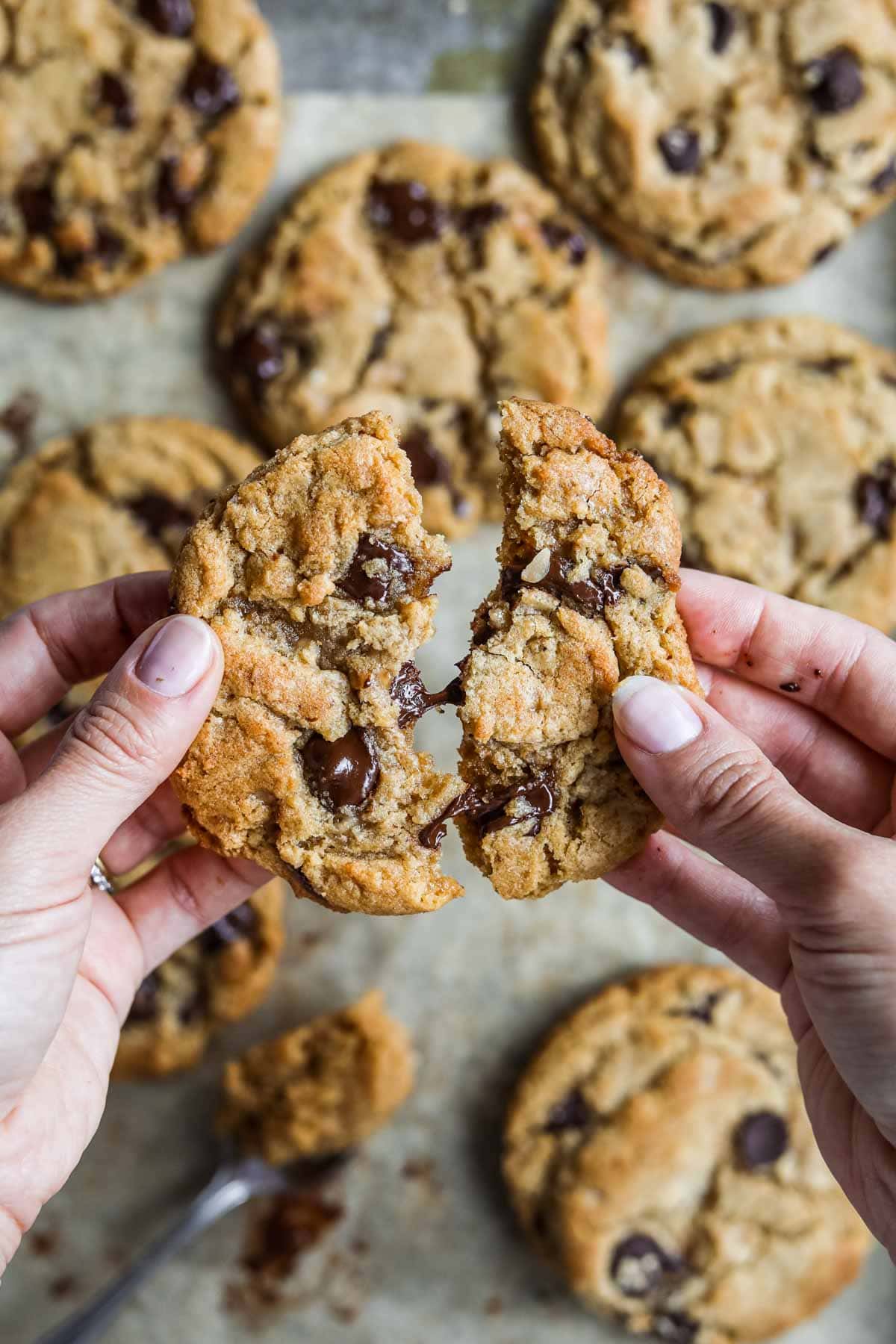 Hands breaking apart a miso toffee browned butter chocolate chip cookies with warm melted chocolate in the center.