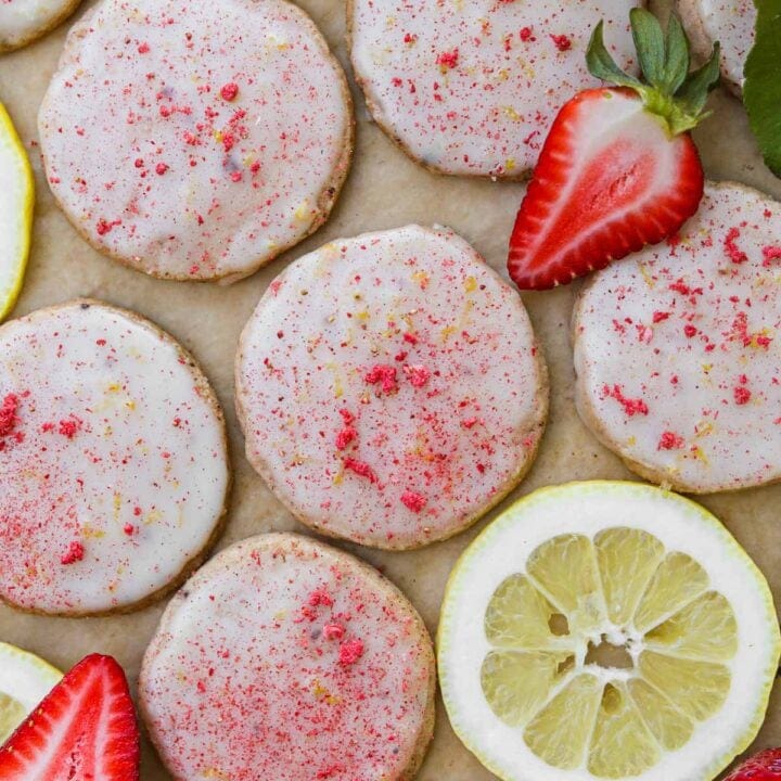 Strawberry lemonade shortbread cookies made with dehydrated strawberries, topped with a lemon glaze, and decorated with fresh strawberries and lemons.