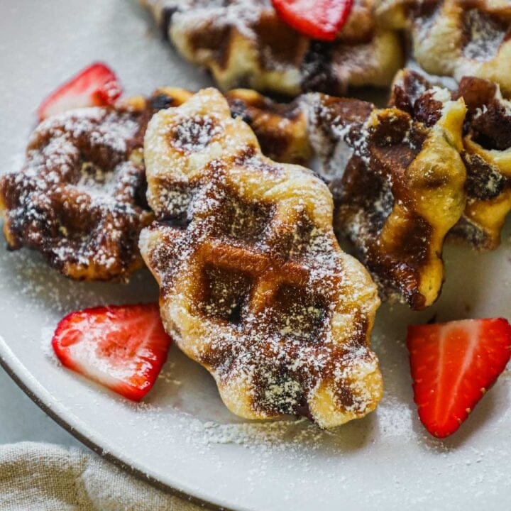 Crispy croffles (croissant waffles) stuffed with Nutella and strawberries and dusted with powdered sugar on a plate.