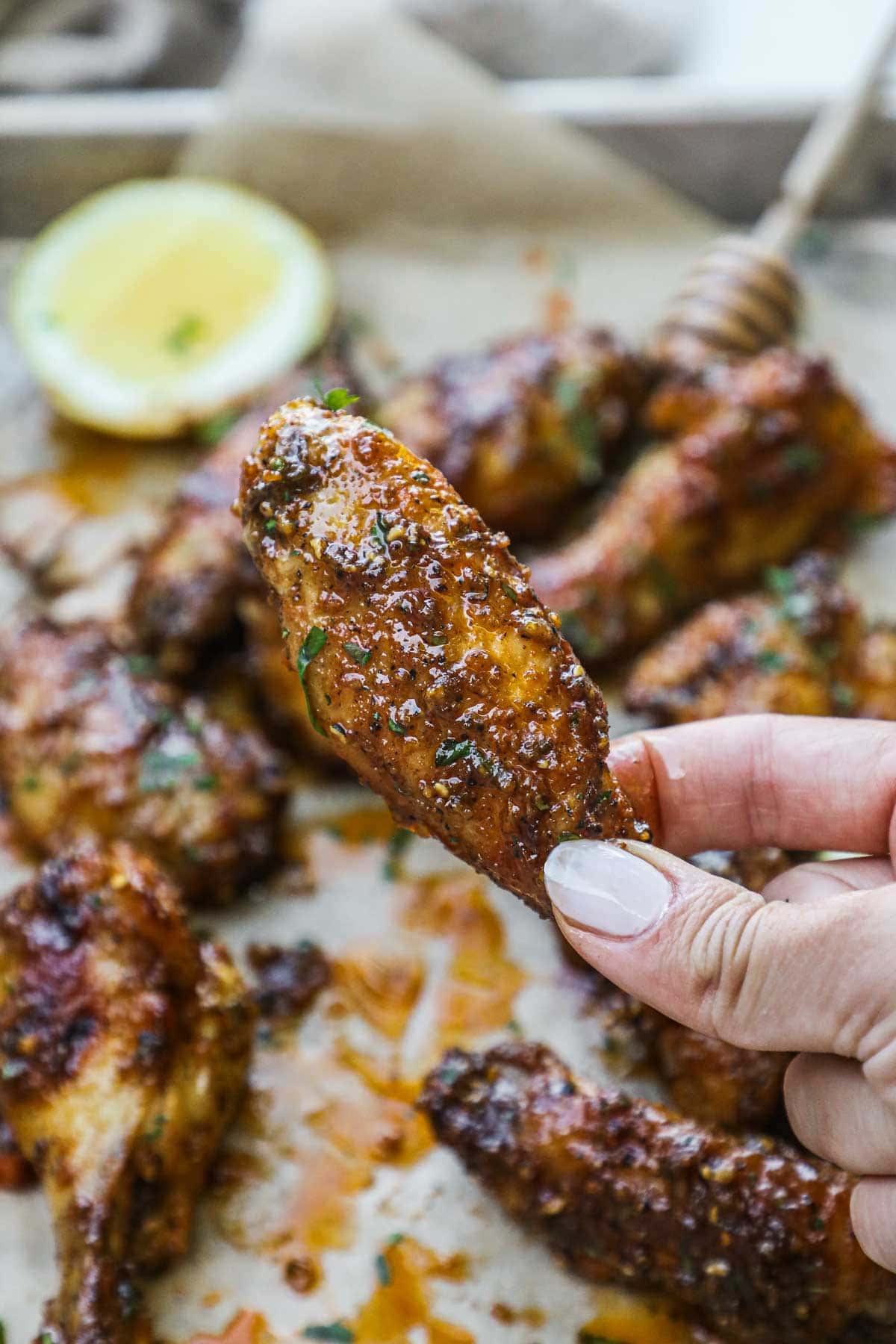 Hand holding a honey lemon pepper flat wing with lots of sauce and parsley.