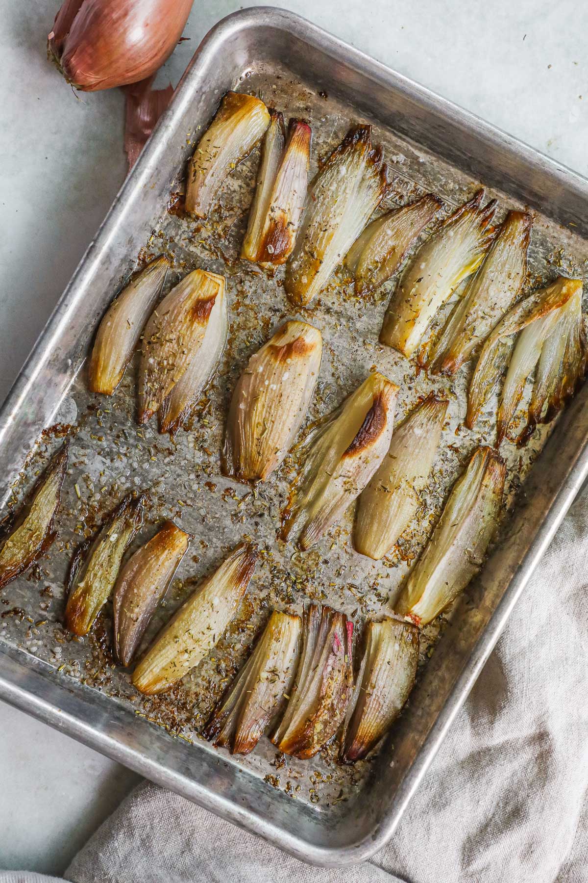 Roasted caramelized shallots on a baking sheet with dried herbs.