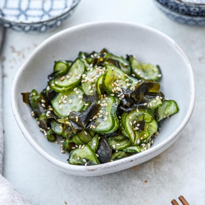 Sunomono (Japanese cucumber salad) with wakame seaweed and sesame seeds in a ceramic bowl with chopsticks.