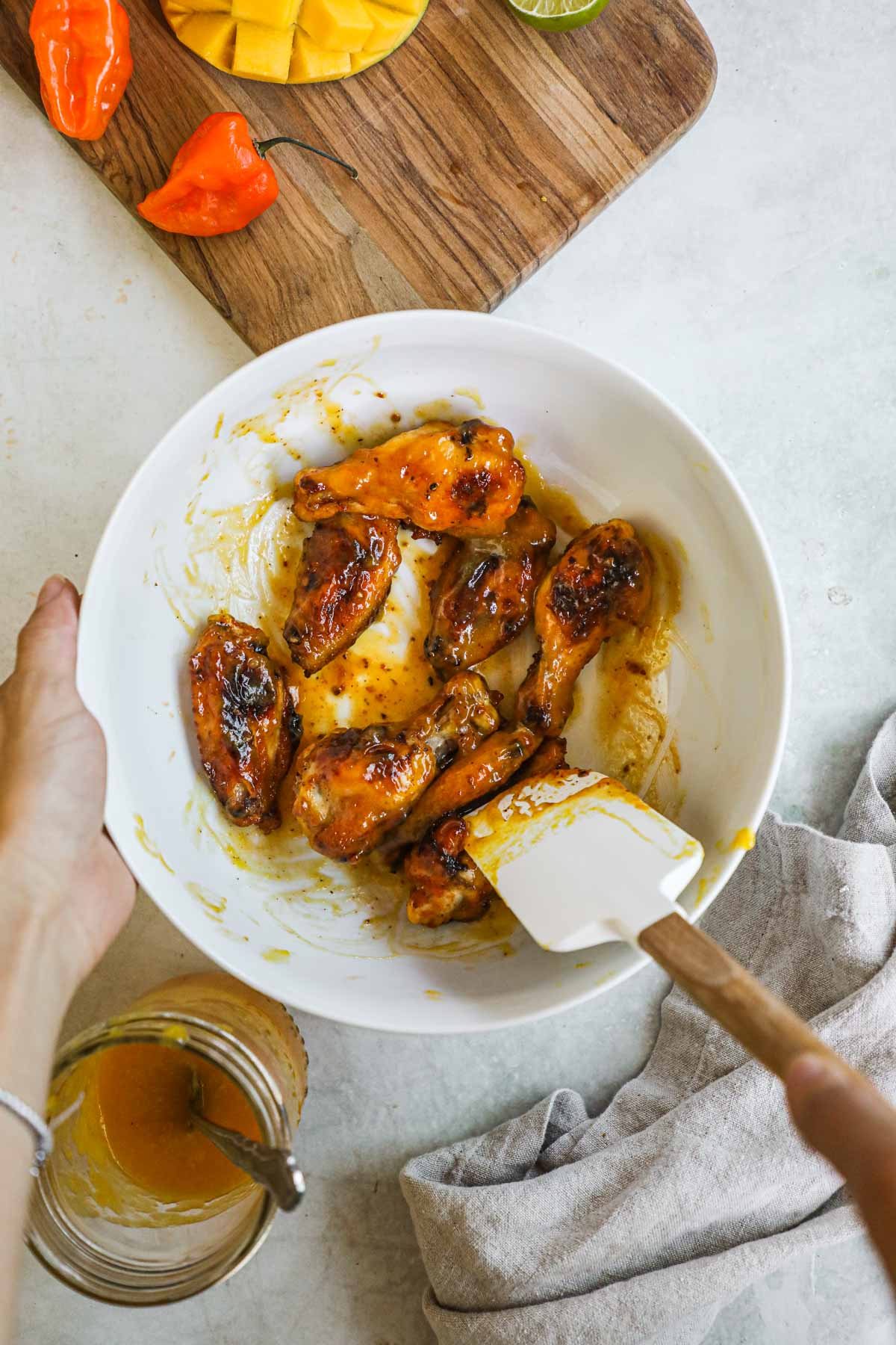 Cooked chicken wings tossed in mango habanero sauce in a white mixing bowl.
