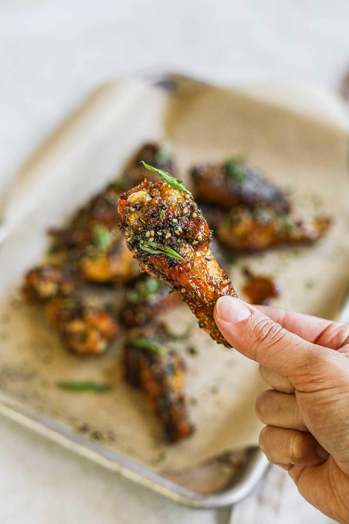 Hand holding a sticky, sweet teriyaki chicken wing with furikake.