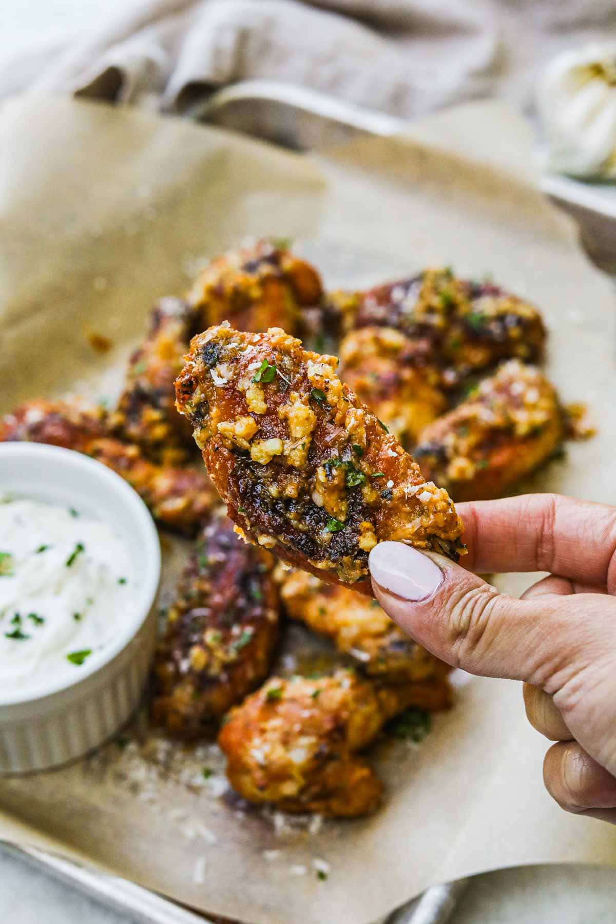 Hand holding garlic parmesan chicken wing flat with a garlic dipping sauce.