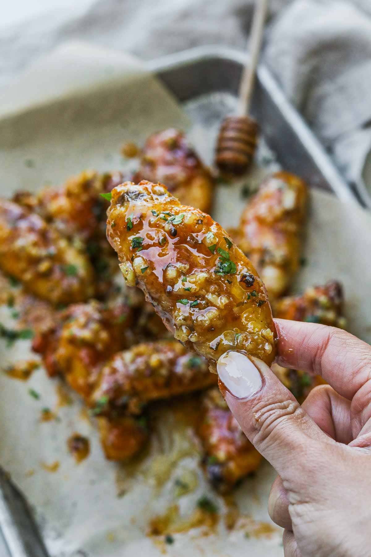 Hand holding a juicy honey garlic chicken wing covered in a homemade sauce.