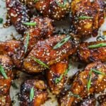 Sweet and sticky honey soy garlic chicken wings on a platter with sliced green onions and sesame seeds.