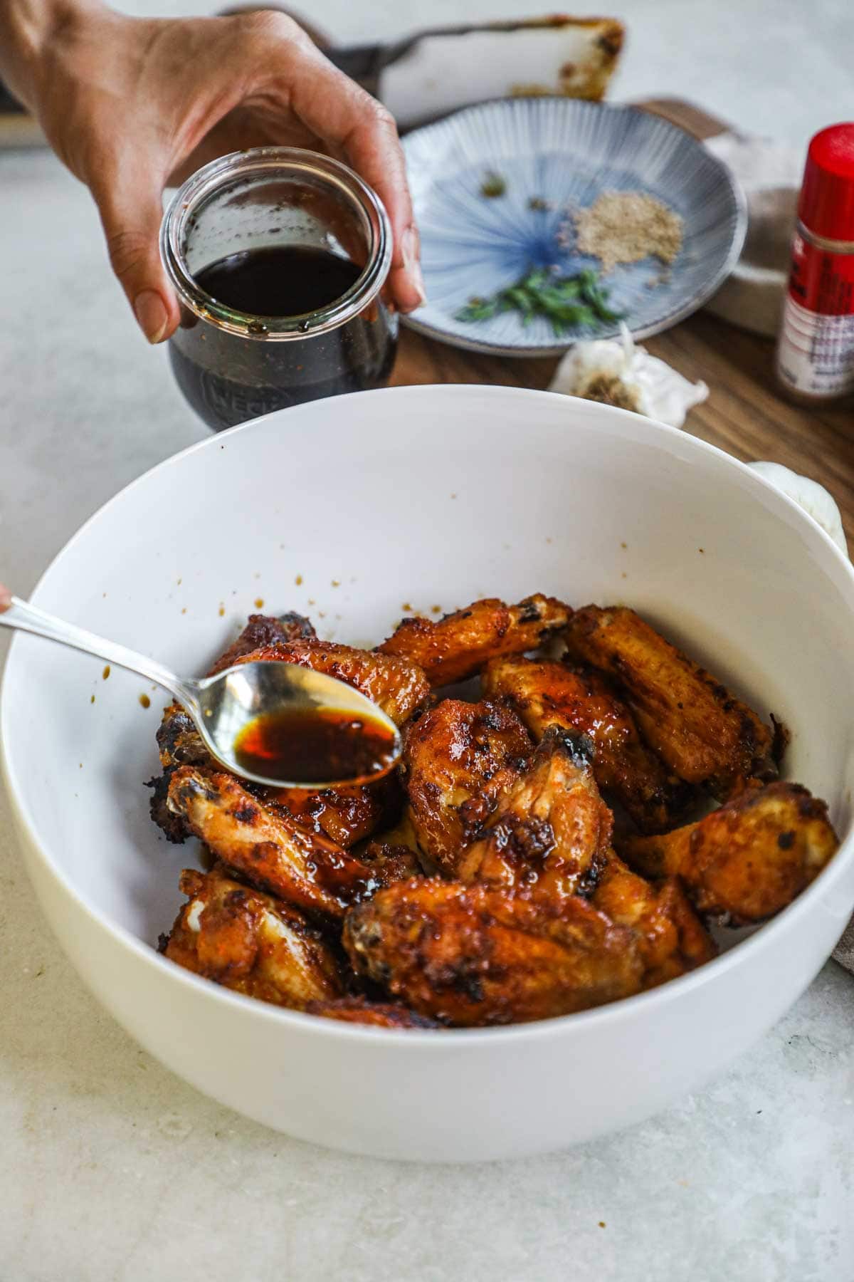 Spoon pouring honey soy garlic sauce on top of cooked wings to make a sticky, umami-packed glaze.