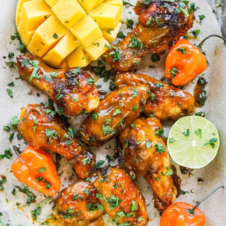 Pile of mango habanero chicken wings on a serving platter with habanero peppers, lime, cilantro, and mango.