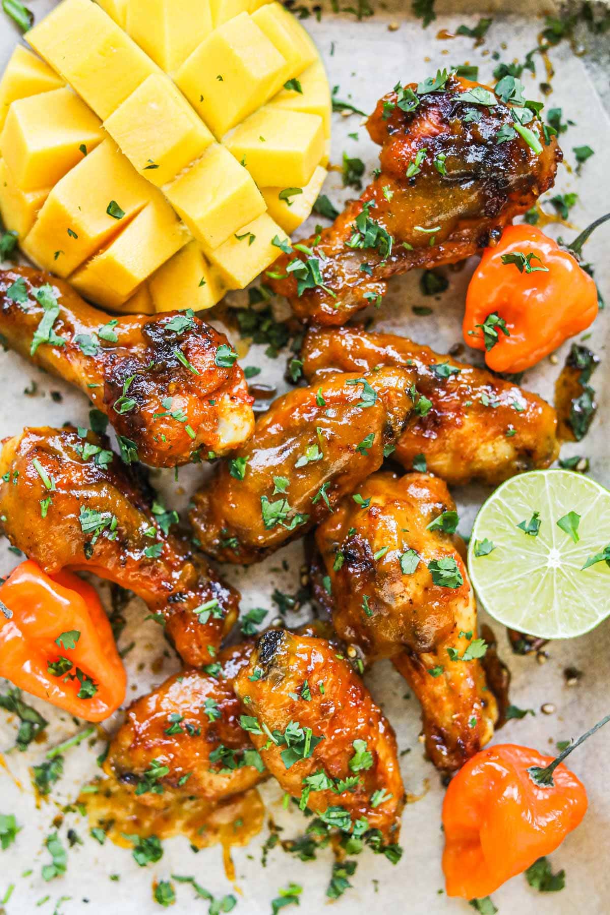 Pile of mango habanero chicken wings on a serving platter with habanero peppers, lime, cilantro, and mango.