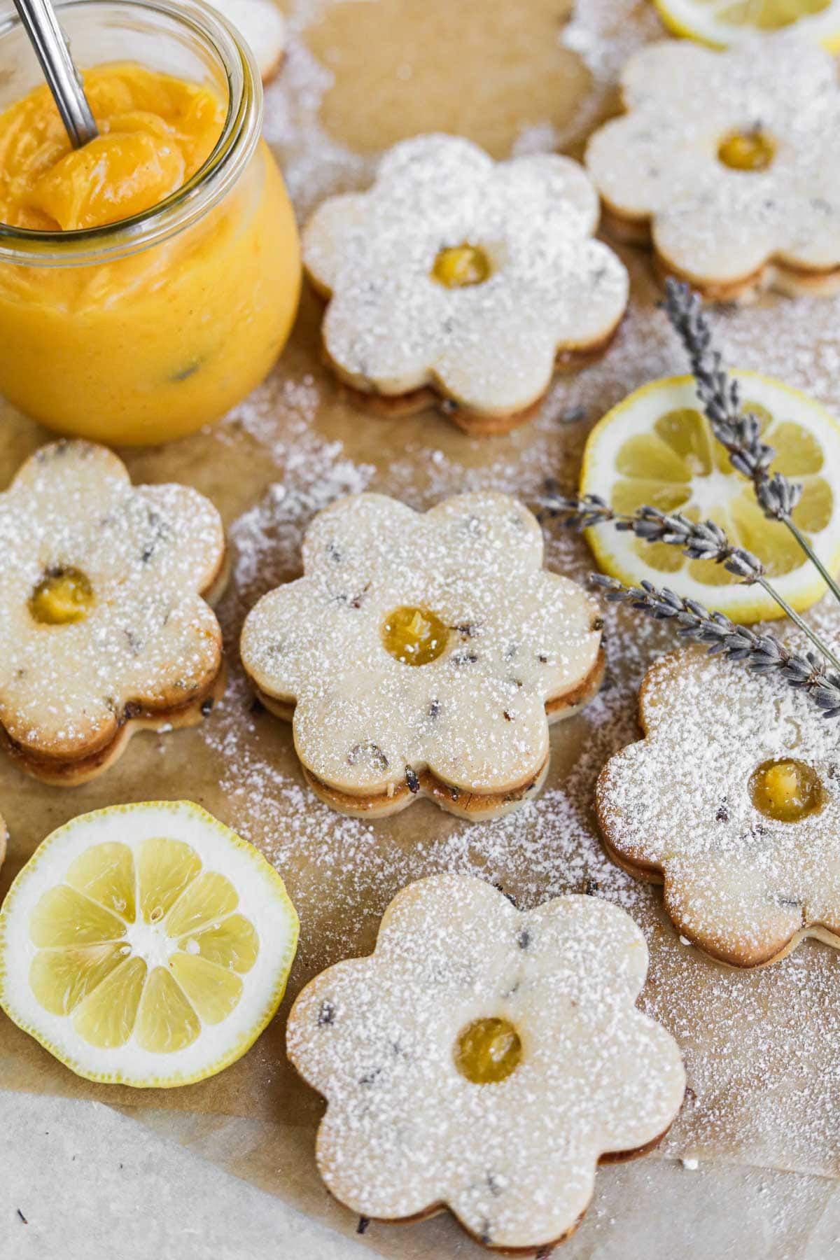 Lavender lemon cookies filled with lemon curd on a sheet of parchment paper with lemon slices and a jar of homemade lemon curd.