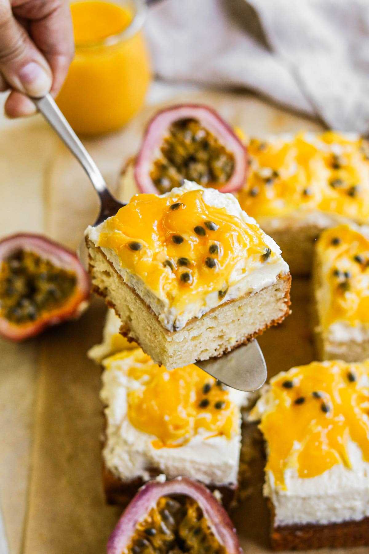 Cake server holding a slice of fluffy sour cream cake topped with mascarpone frosting, passion fruit curd, and fresh passion fruit pulp.