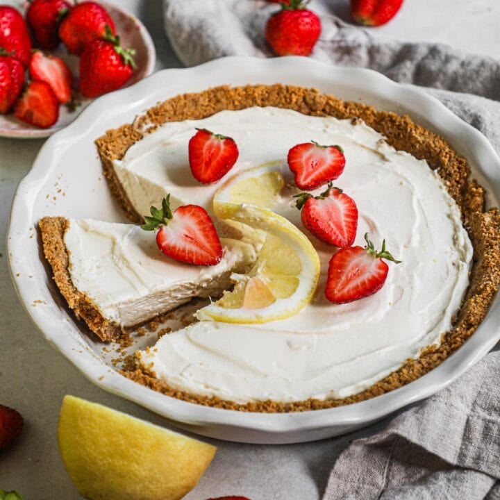 3-ingredient no bake cheesecake made with whipped cream, cream cheese, and powdered sugar in a premade graham cracker crust in a pie pan topped with fresh strawberries and lemon.