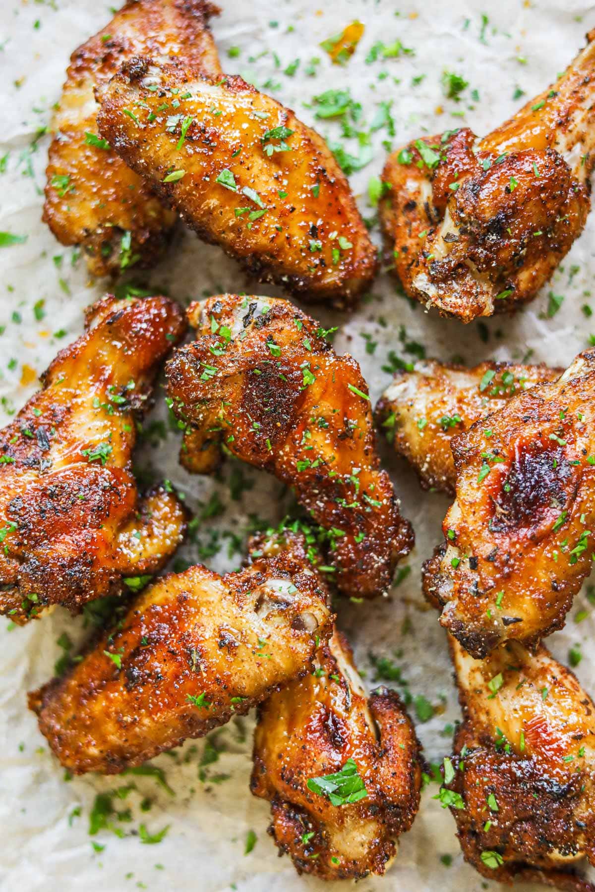 Baked dry rub chicken wings made with a brown sugar rub topped with finely chopped parsley on a sheet of parchment paper.