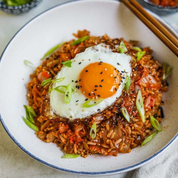 Easy kimchi fried rice in a bowl with a fried egg, sesame seeds, and scallions on top with chopsticks.