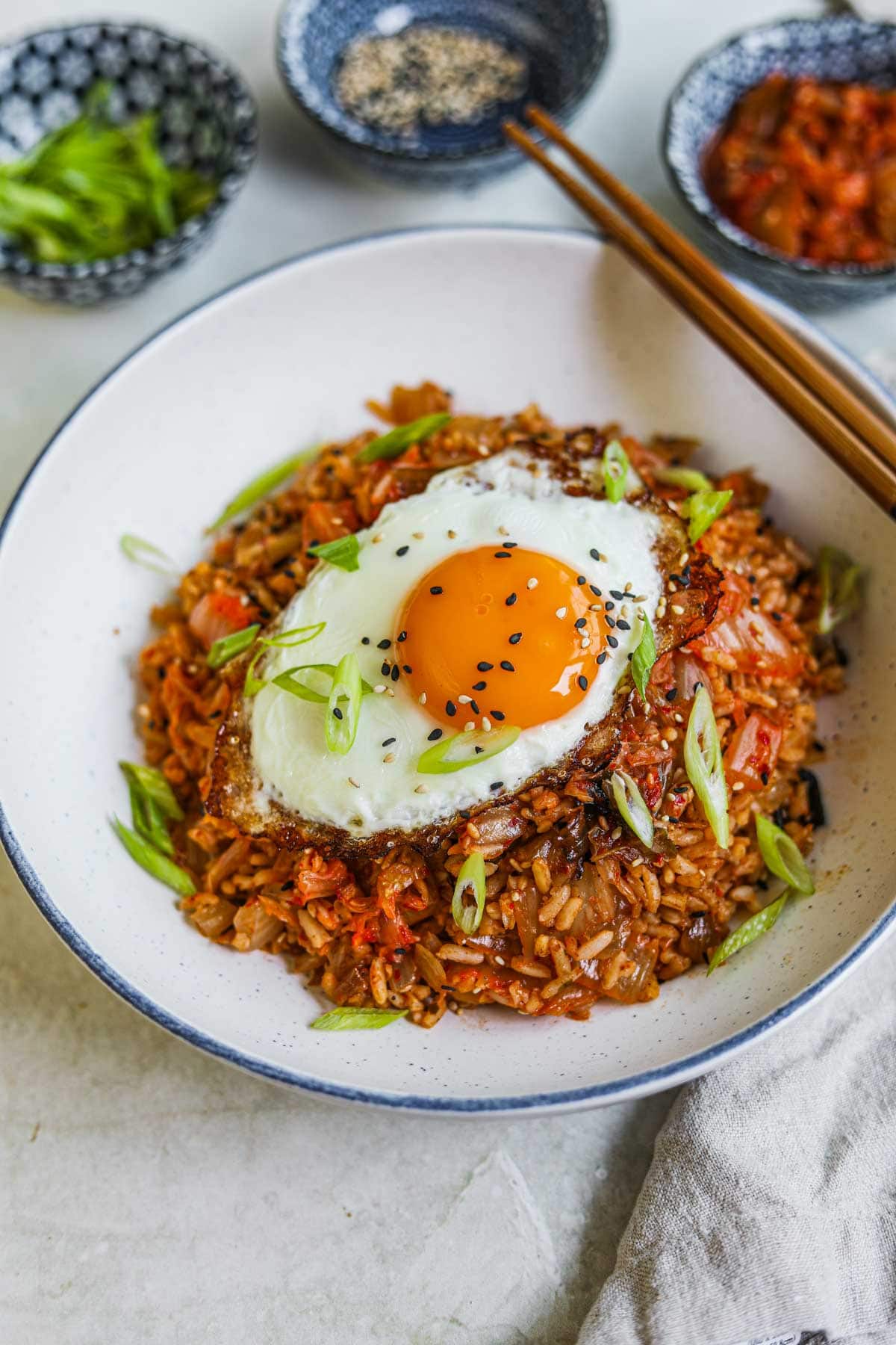 Easy kimchi fried rice in a bowl with a fried egg, sesame seeds, and scallions on top with chopsticks.