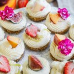 No-bake mini cheesecakes topped with fresh fruit, edible flowers, powdered sugar on a marble platter.