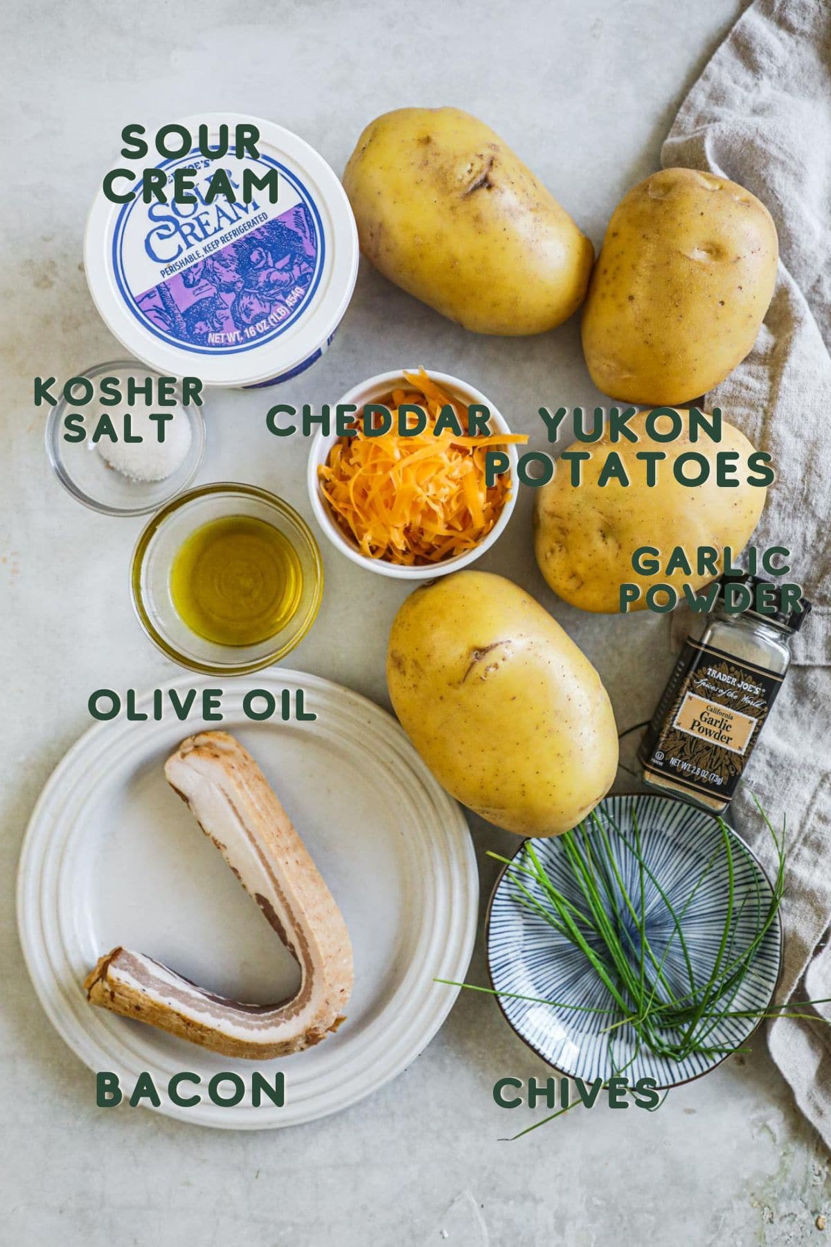 Ingredients to make hasselback potatoes, sour cream, kosher salt, yukon potatoes, cheddar, olive oil, garlic powder, chives, bacon.
