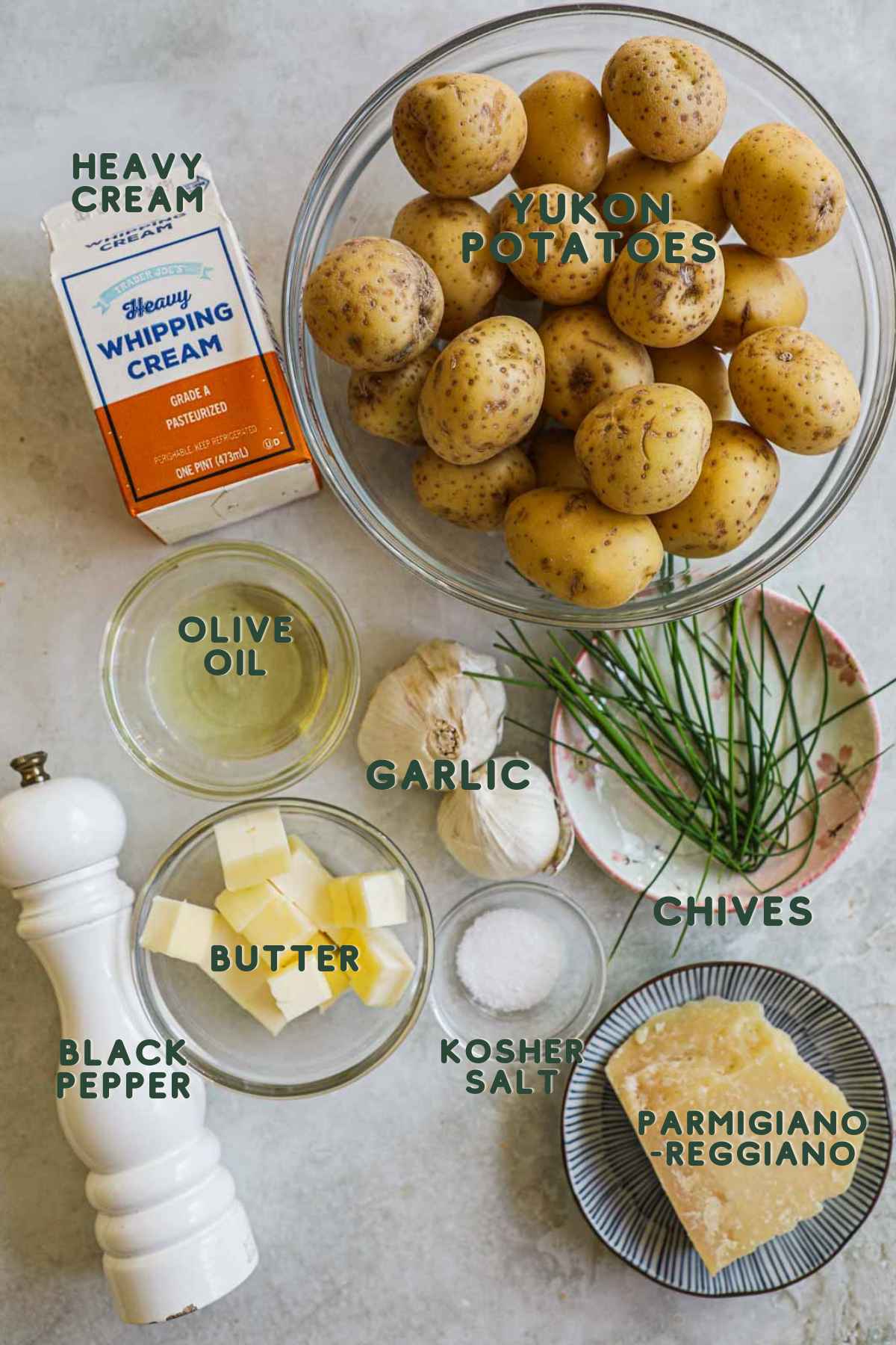 Ingredients to make roasted garlic mashed potatoes, yukon potatoes, heavy cream, olive oil, garlic, chives, butter, parmigiano-reggiano, pepper, kosher salt.