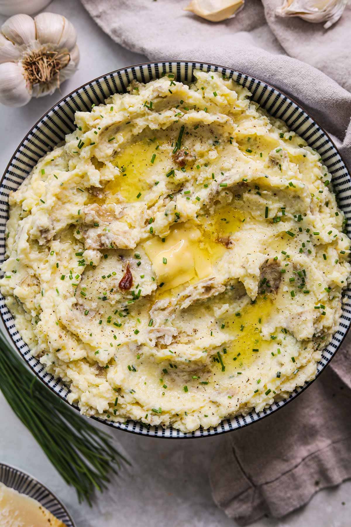 Roasted garlic yukon mashed potatoes with parmigiano-reggiano, sour cream, creamy roasted garlic, and chives in a striped blue and white bowl.