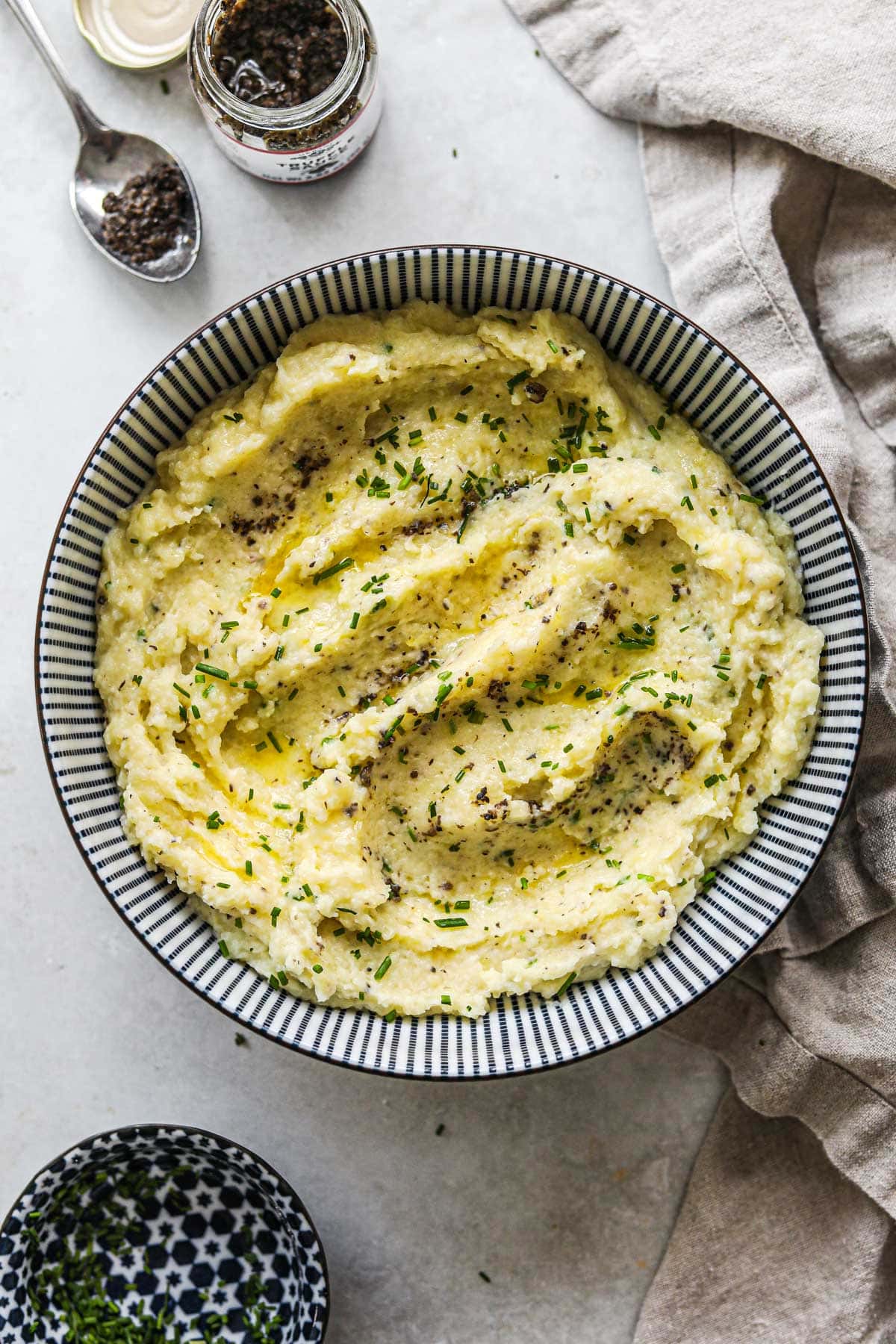 Creamy truffle mashed potatoes with creme fraiche and chives in a bowl with flecks of truffle puree in the potatoes.