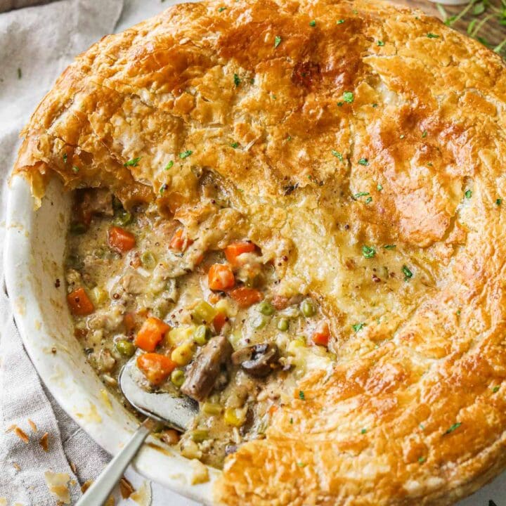 Golden, crispy vegetarian pot pie in a pie dish filled with carrots, corn, peas, onion, and celery with a spoon in the filling.