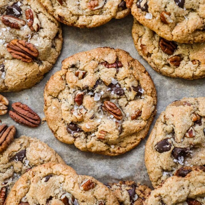 Warm and chewy browned butter pecan chocolate chip cookies with flaky sea salt on a parchment paper-lined baking sheet.