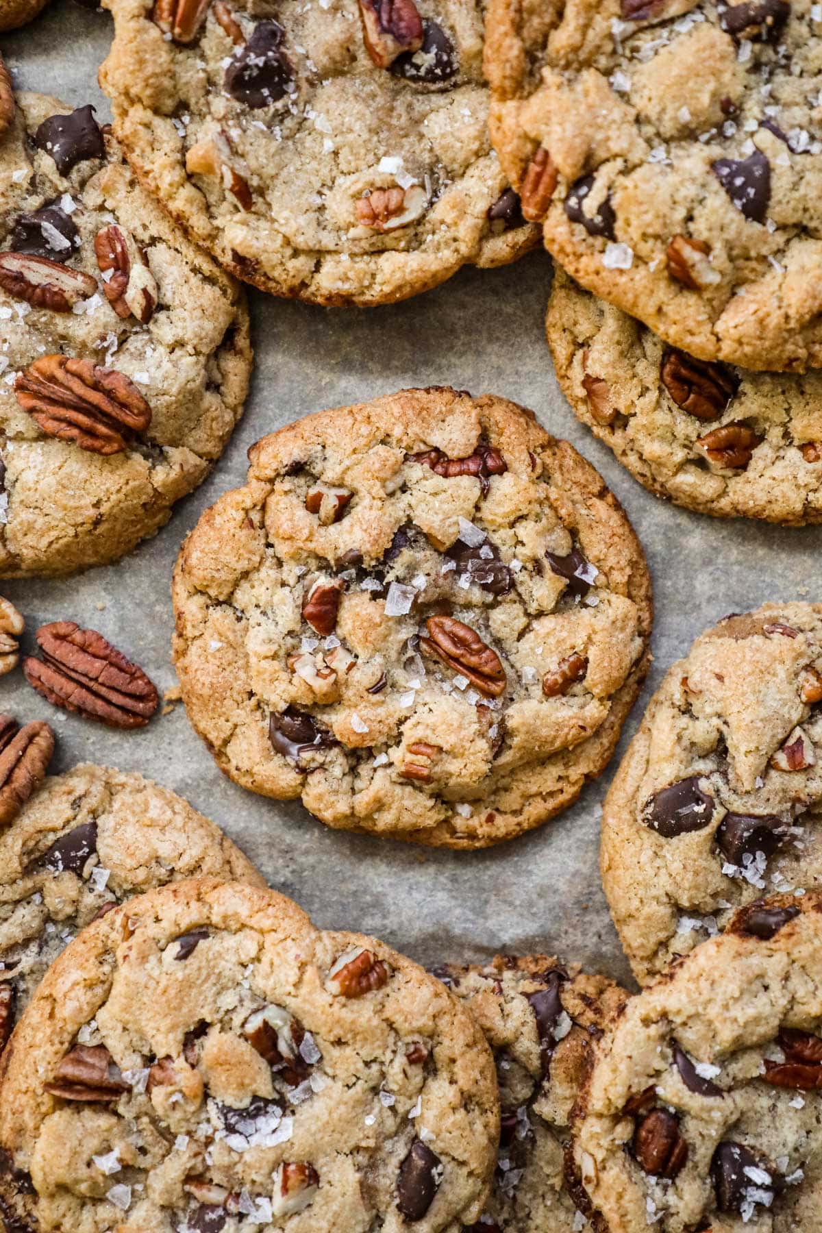 Warm and chewy browned butter pecan chocolate chip cookies with flaky sea salt on a parchment paper-lined baking sheet.