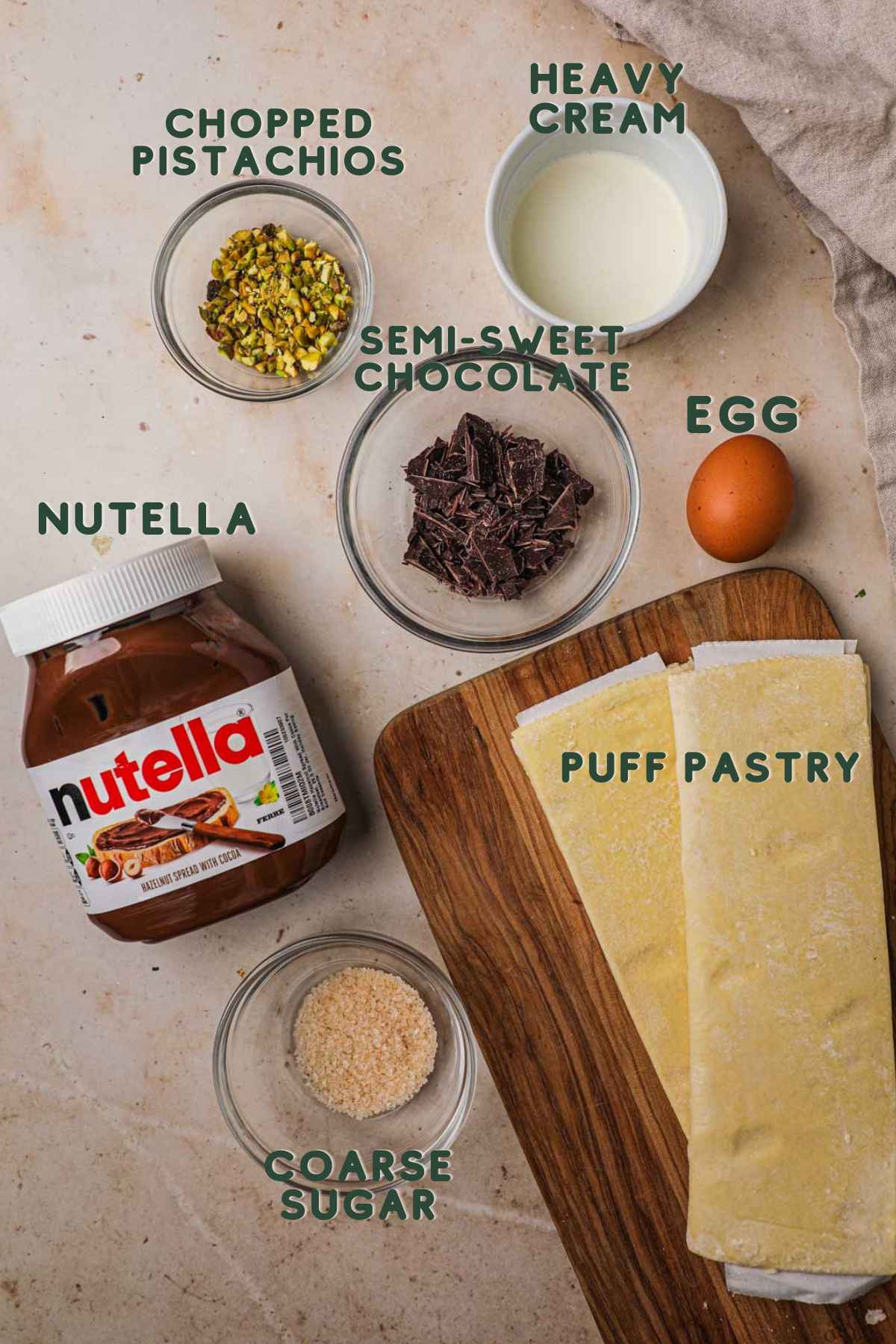 Ingredients to make chocolate twists, puff pastry, semi-sweet chocolate, nutella, egg, heavy cream, chopped pistachio, coarse sugar.