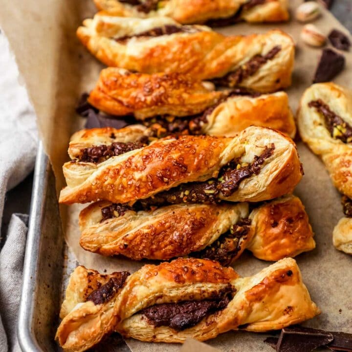 Puff pastry twists stuffed with Nutella, dark chocolate, and chopped pistachios lined on a parchment paper-lined baking sheet.