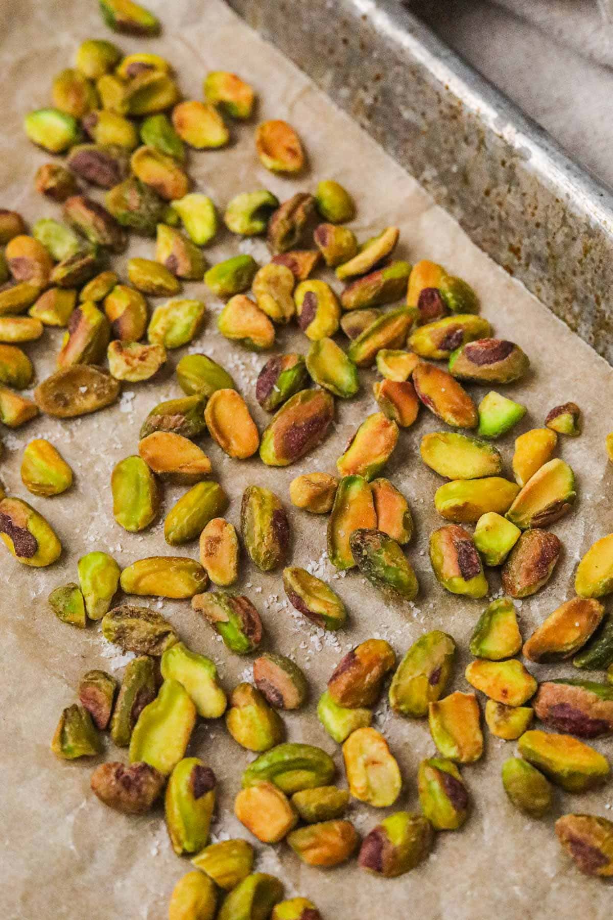 Roasted green pistachios with sea salt on a parchment paper-lined baking sheet.