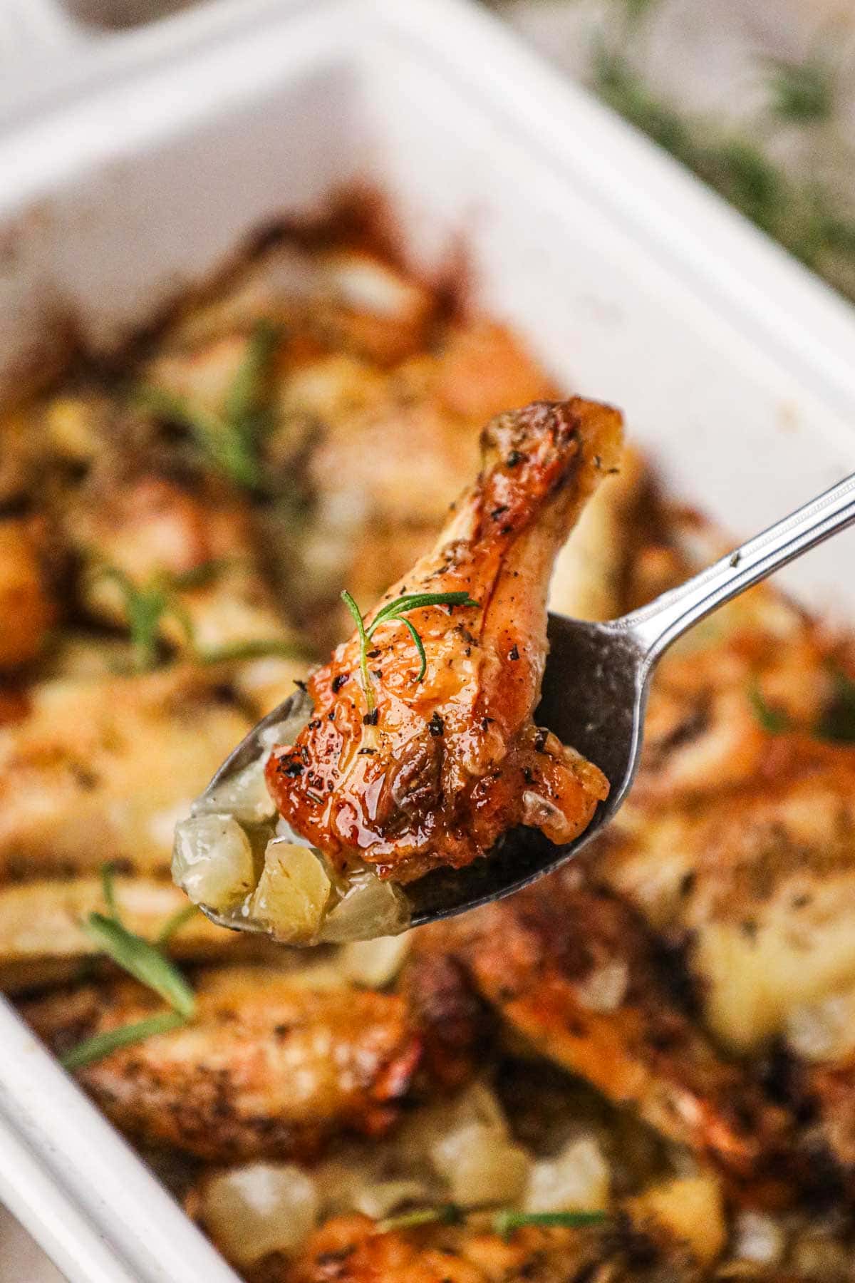 Spoon scooping up an Italian chicken wing and softened onions, bathed in a mixture of fresh rosemary, olive oil, and dry white wine.