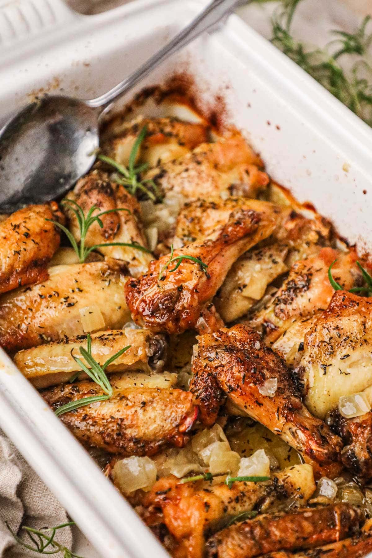 Baked Italian rosemary chicken wings with golden skin made with white wine and cooked on top of a bed of onions.