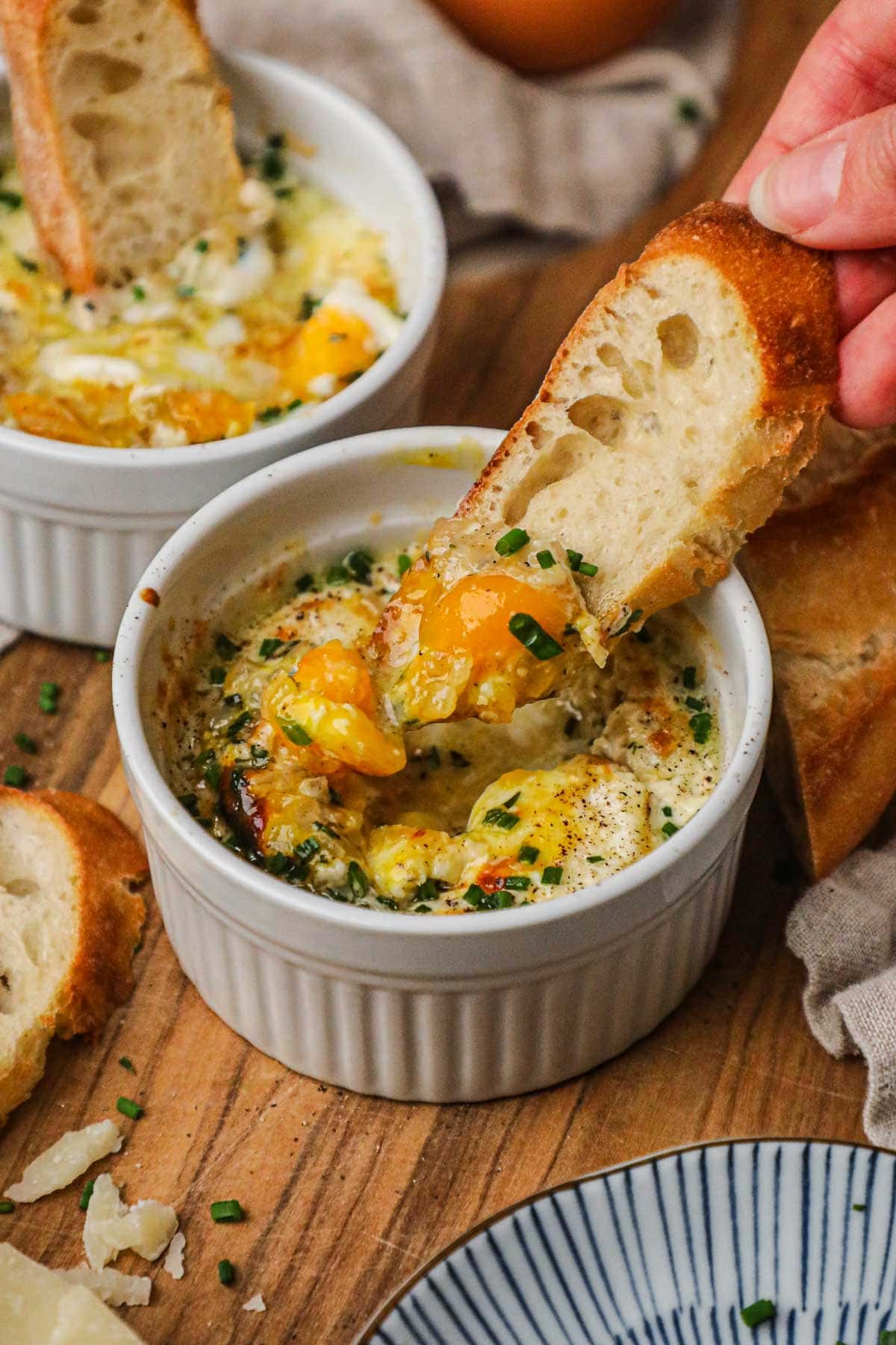 Hand dipping baguette in creamy, cheesy baked eggs with shallots and herbs.