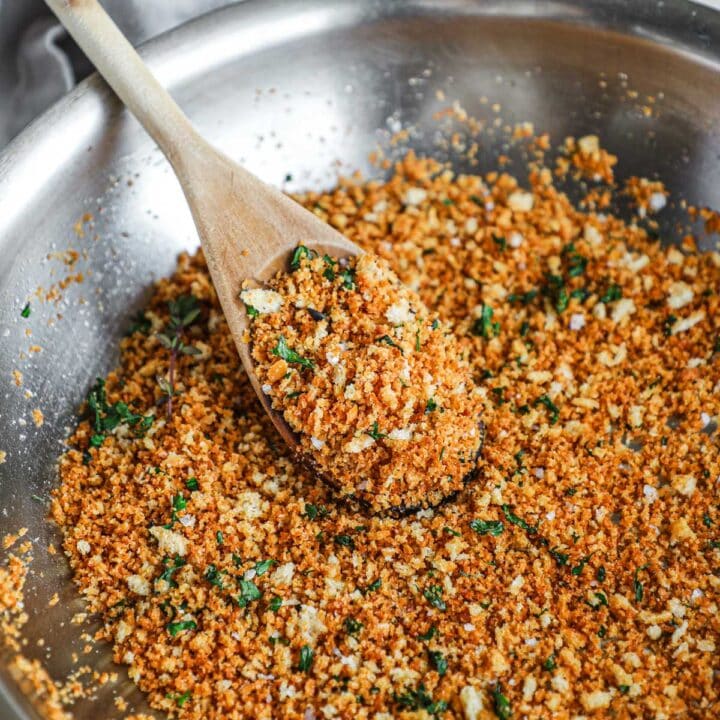 Herbed pangrattato in a pan with an Italian wooden spoon holding a scoop of crispy breadcrumbs.