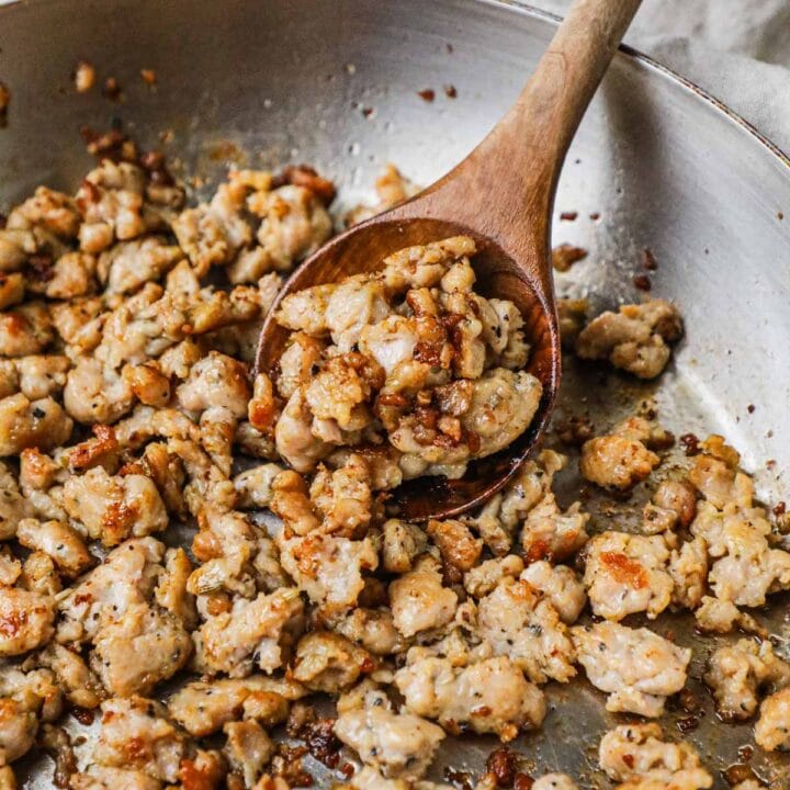 Caramelized and browned ground Italian sausage in a pan with a wooden spoon holding a scoop.