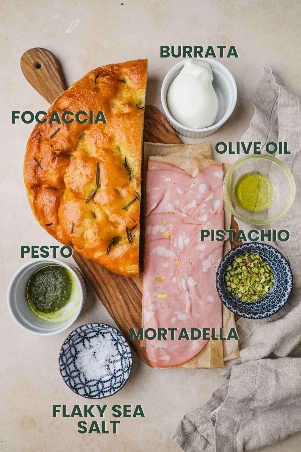 Ingredients for a mortadella panino, focaccia, burrata, olive oil, mortadella, pistachio, flaky sea salt, pesto.