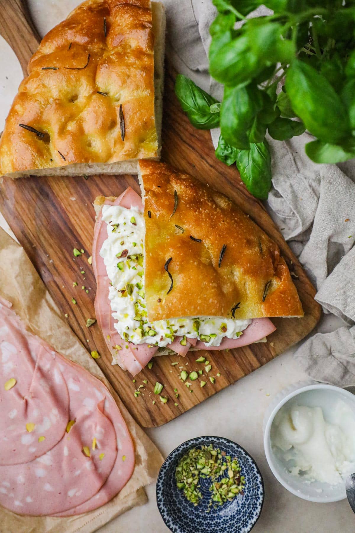 Overhead photo of a homemade mortadella panino, filled with burrata, pistachio, pesto, and layers of thinly sliced mortadella