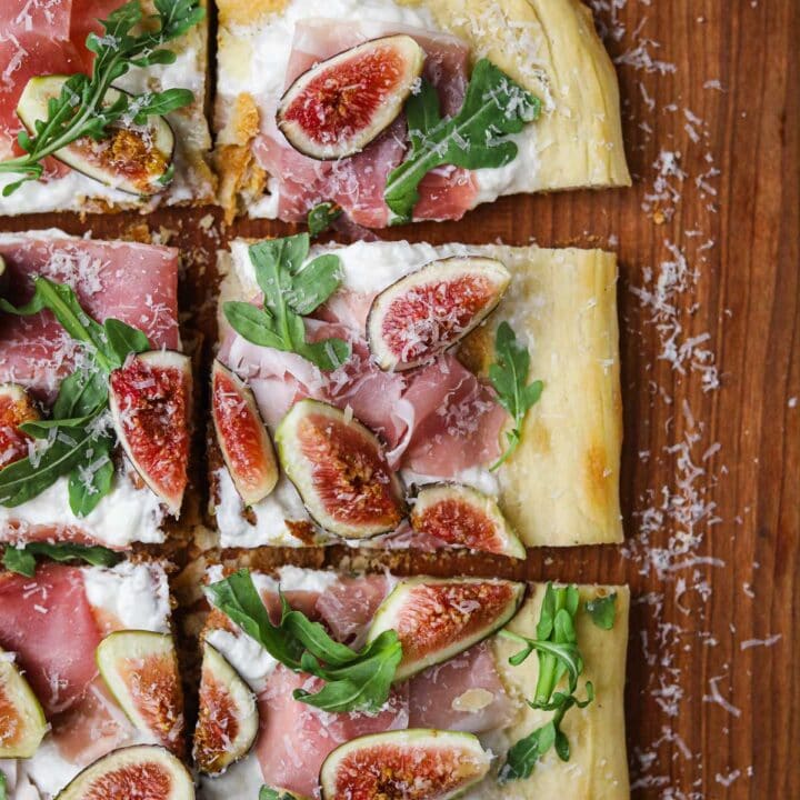 White pizza with fig, prosciutto, arugula, and burrata on a wooden serving board.