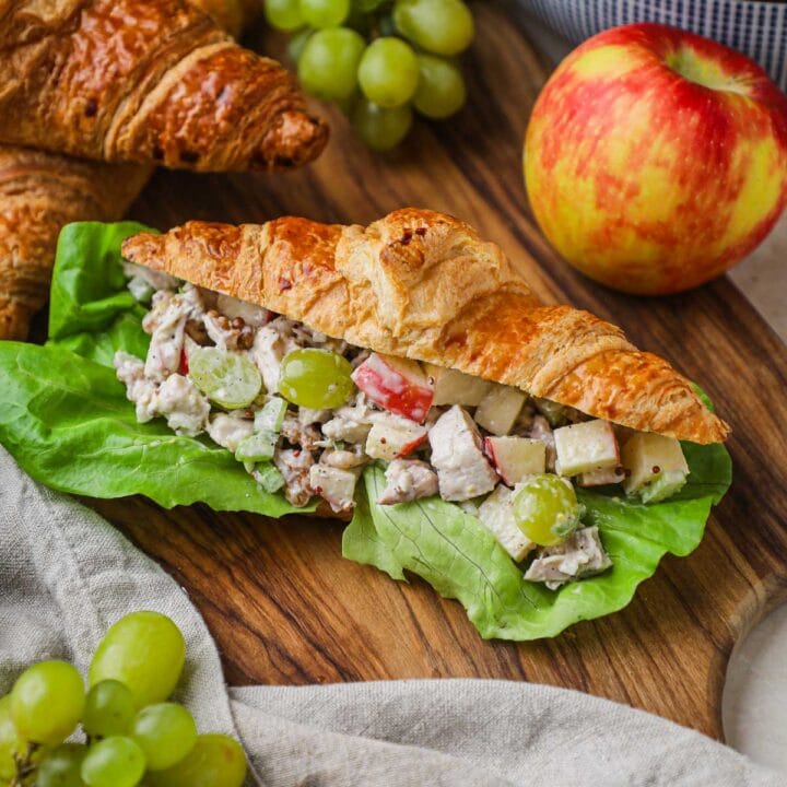 Chicken salad croissant sandwich with lettuce and rotisserie chicken served on a wood board for a healthy lunch.