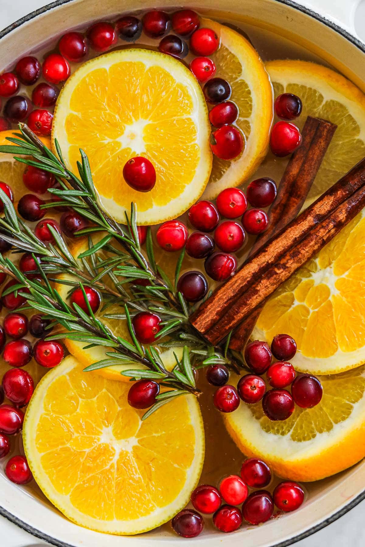 Christmas stovetop potpourri with fresh cranberries, rosemary, cinnamon sticks, and fresh sliced oranges in a Le Creuset dutch oven that deodorizes and adds a fresh scent to a home.