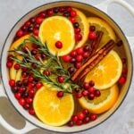 Christmas stovetop potpourri with fresh cranberries, rosemary, cinnamon sticks, and fresh sliced oranges in a Le Creuset dutch oven that deodorizes and adds a fresh scent to a home.