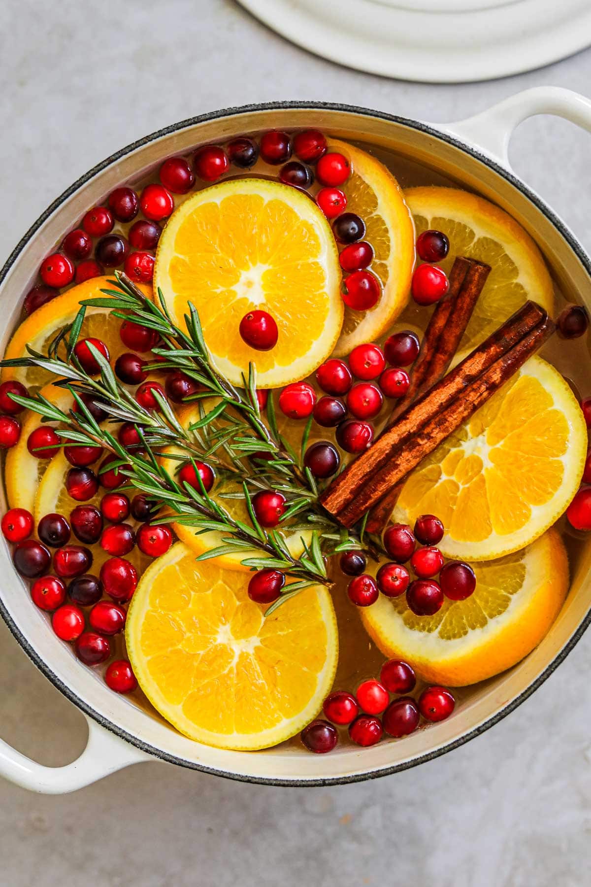 To make a winter stovetop simmer pot, add sliced oranges, fresh sprigs of rosemary, cinnamon sticks, and fresh cranberries to a pot with water, then bring to a simmer until fragrant.