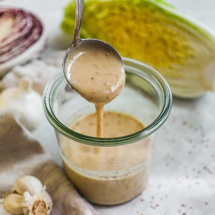 Ladle pouring a scoop of Asian honey sesame dressing in a glass jar.